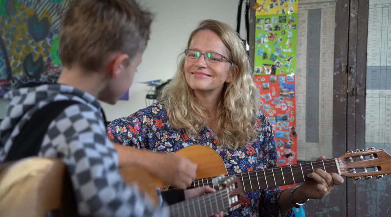 Mai van der Beele speelt gitaar tijdens een muziektherapiesessie met een jongere